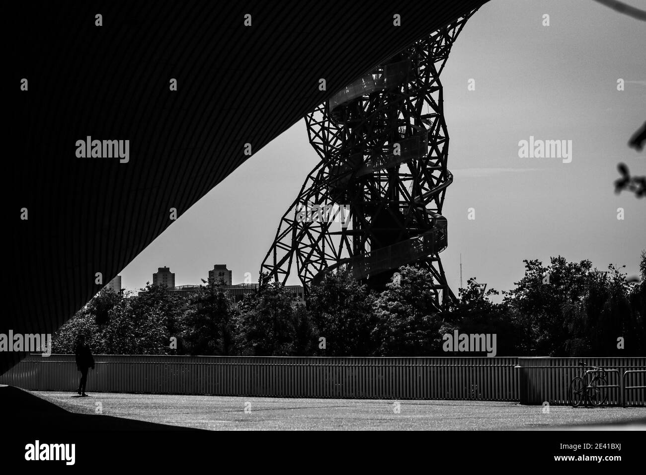 A single person stands, dwarfed by the London Olympic aquatics centre, with the ArcelorMittal Orbit tower in the background. Stock Photo