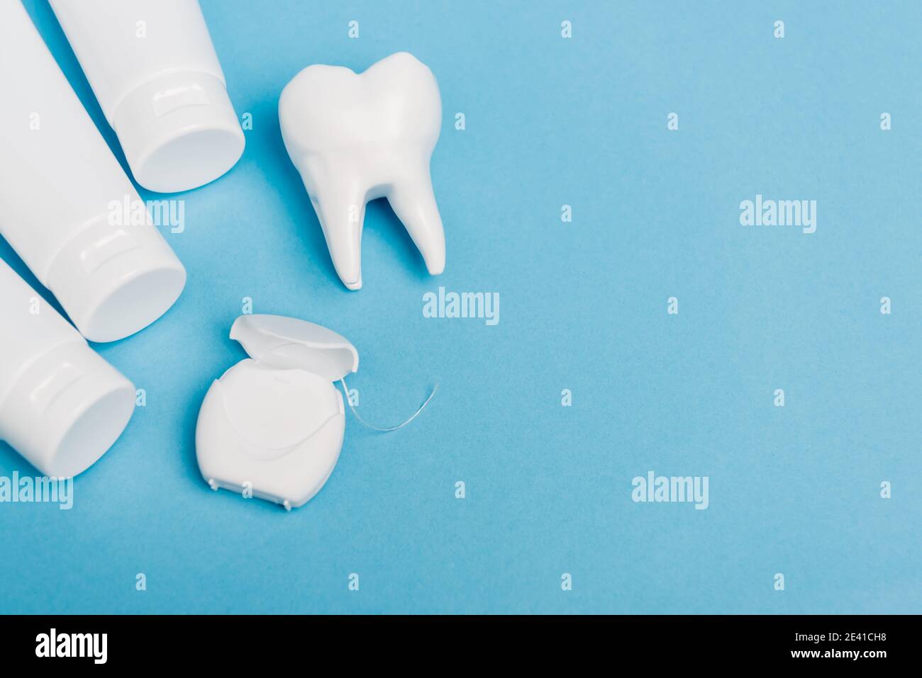 Top view of dental floss near tooth model and tubes with toothpaste on ...