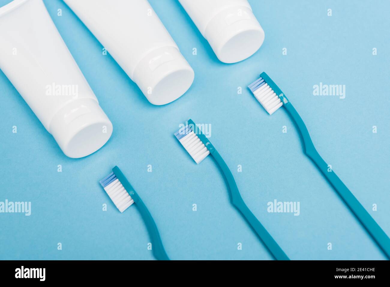 Top view of toothbrushes near tubes with toothpaste on blue background ...