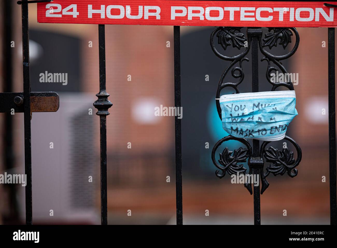24 hour protection ... a locked gate with a face mask with the words 'You must wear a face mask to enter here' written on it Stock Photo