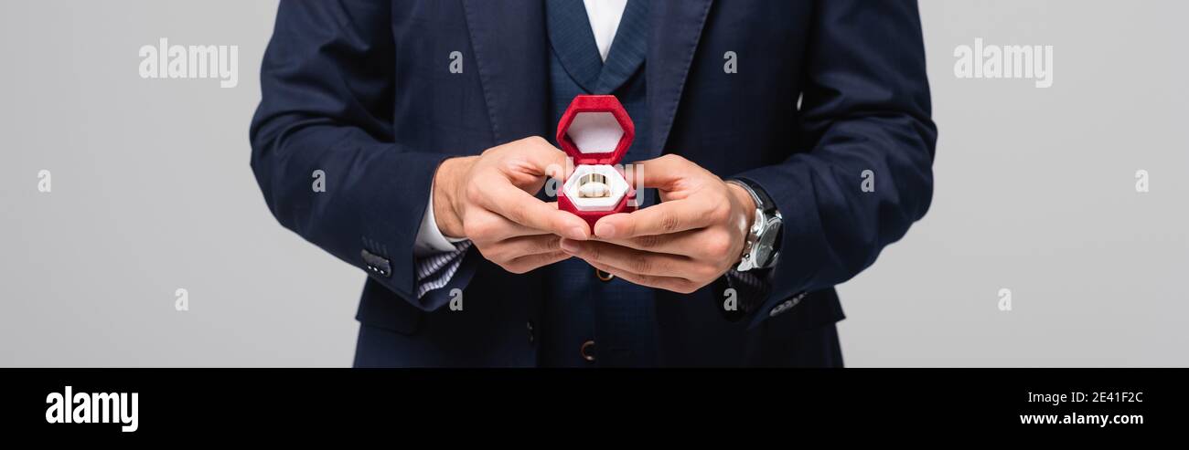 partial view of man in suit holding jewelry box with wedding ring isolated on grey, banner Stock Photo