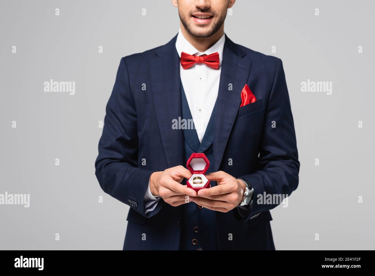 partial view of smiling man in elegant suit holding jewelry box with wedding ring isolated on grey Stock Photo