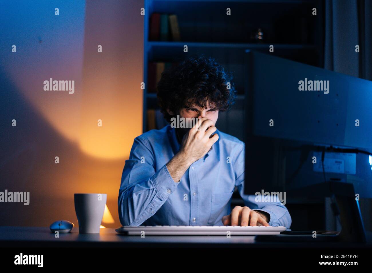 Close-up view of unhappy young man having idea moment pointing finger up while sitting at desk. Stock Photo