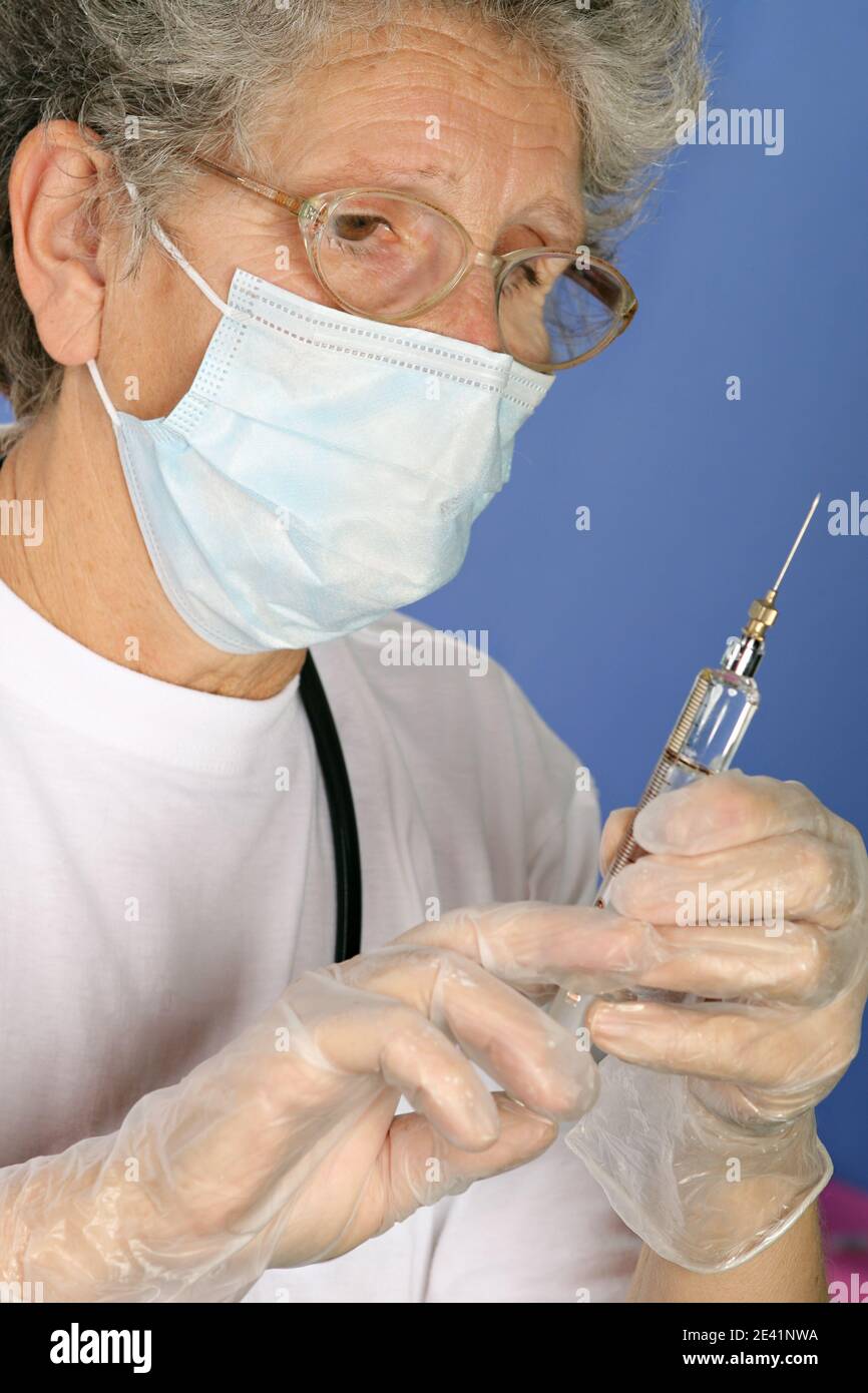 Nurse with protective mask and gloves prepares injection of vaccine or medicine for disease prevention with glass syringe and large needle Stock Photo