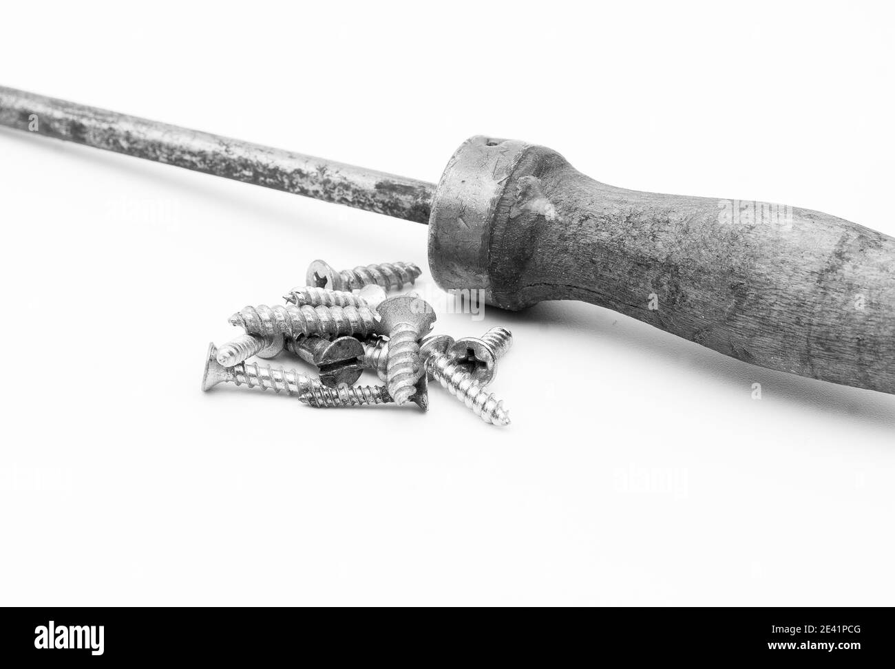 Grayscale shot of metal screws and screwdriver isolated on white background Stock Photo