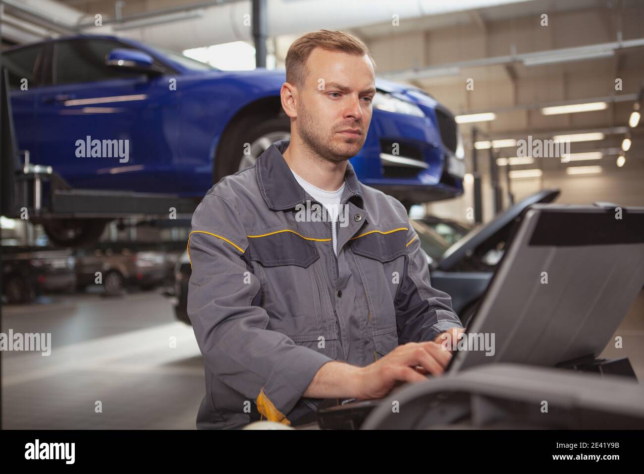 Mature male car mechanic looking concentrated, doing computer diagnostics on a broken automobile at his workshop. Cars, transportation concept Stock Photo