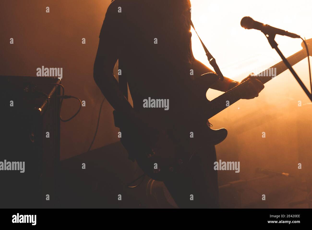 Silhouette of bass guitar player with microphone in bright warm illumination, live music theme Stock Photo