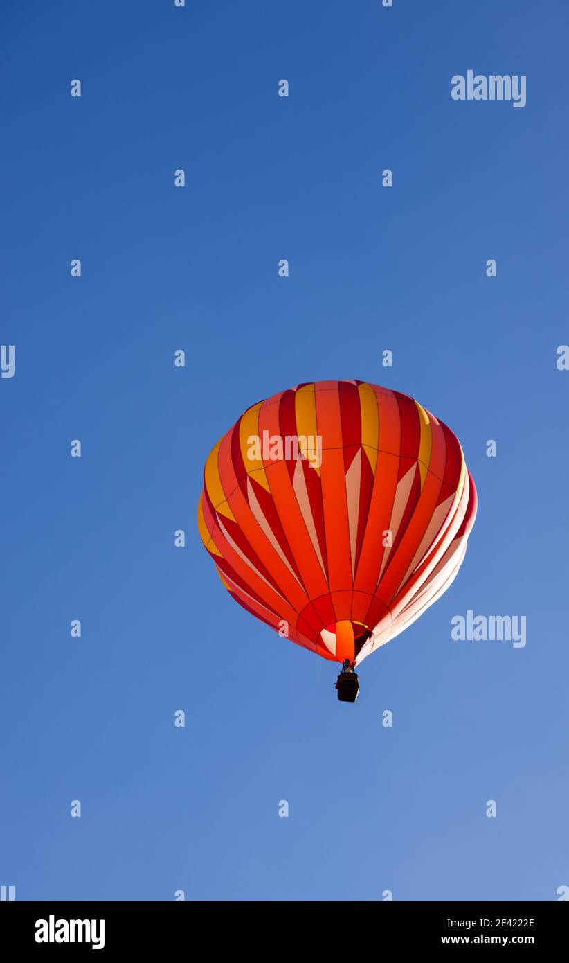 A colorful hot air balloon floating up into the clear blue sky with ...