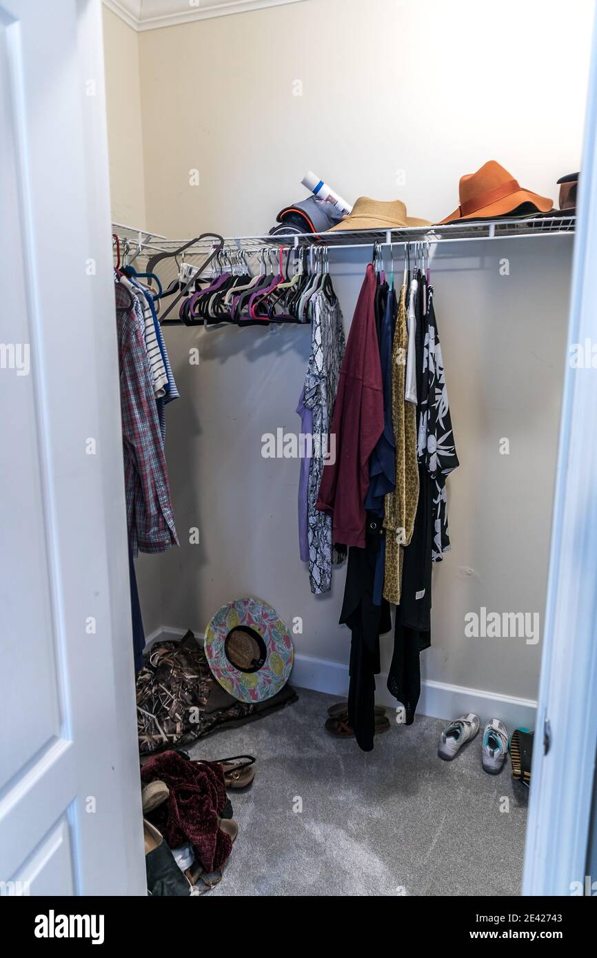 A mostly empty walk in messy closet with some hanging clothes and hats Stock Photo