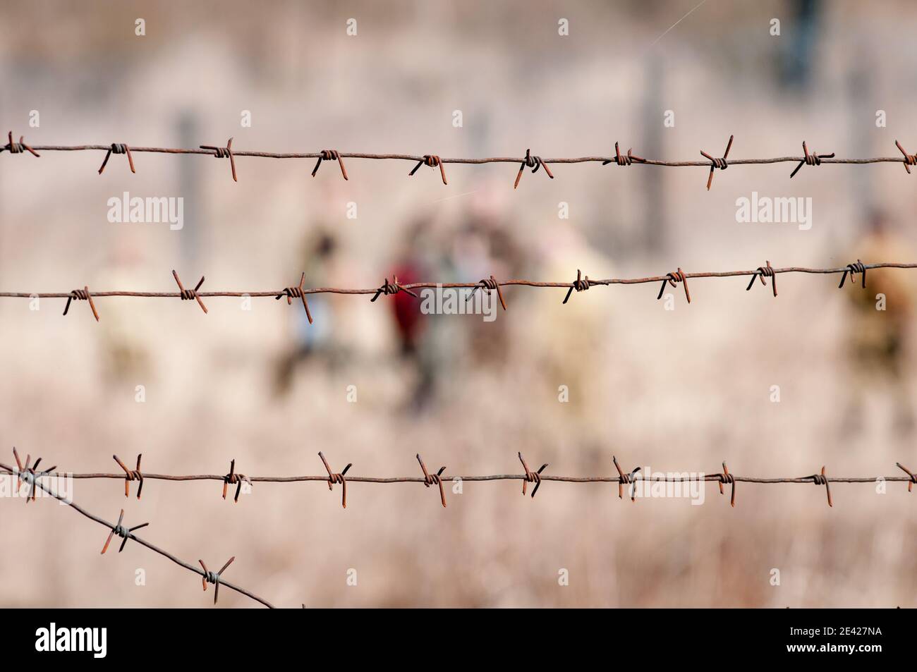 Old rusty barbed wire on the fence and blurred figures of people Stock Photo