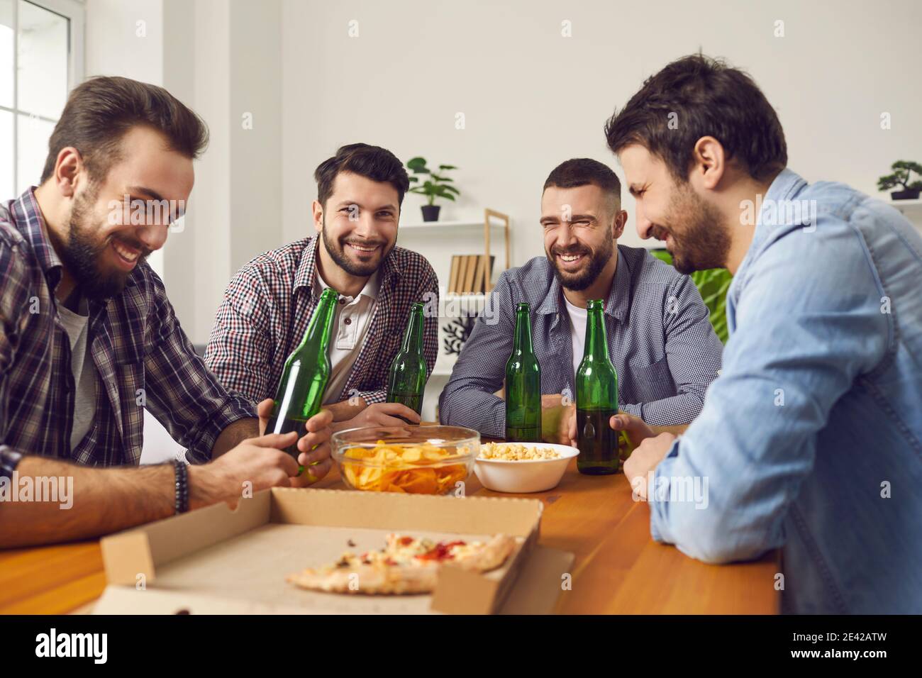 Group of friends eating pizza, drinking beer, telling jokes and having good time Stock Photo
