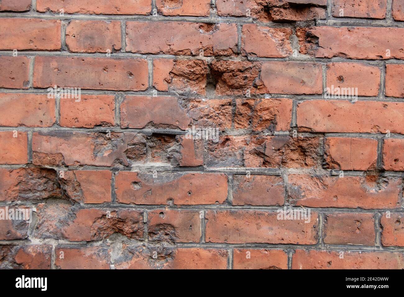 Dark brown old bricks wall with parts knocked out from bullets Stock Photo