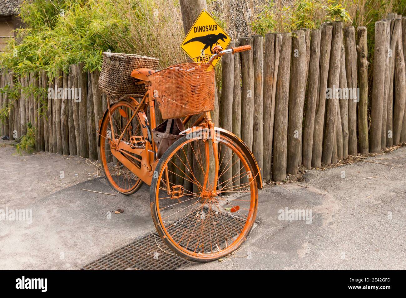 Aalborg, Denmark - 25 Jul 2020: An old orange bicycle is parked up by a wooden fence, signposted with crossing traffic of dinosaurs Stock Photo