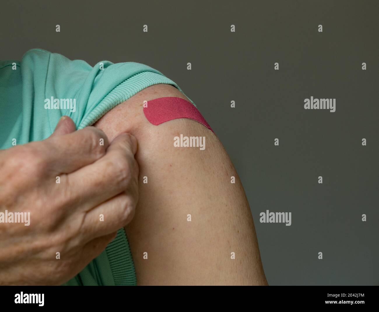 Senior caucasian man holding up shirt sleeve to show the bandaid after coronavirus vaccine shot in the shoulder Stock Photo