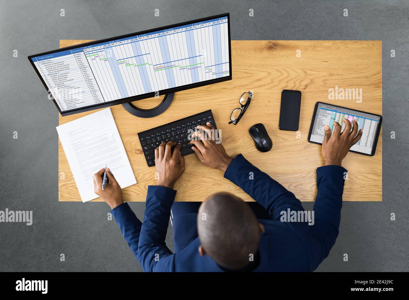 Tired Young African Man Doing Multitasking Work On Laptop In Office Stock Photo
