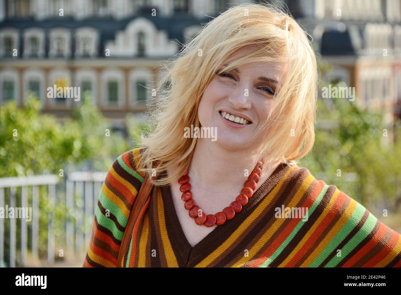 A woman with 1970-style hairstyle and clothes smiles outdoors Stock Photo