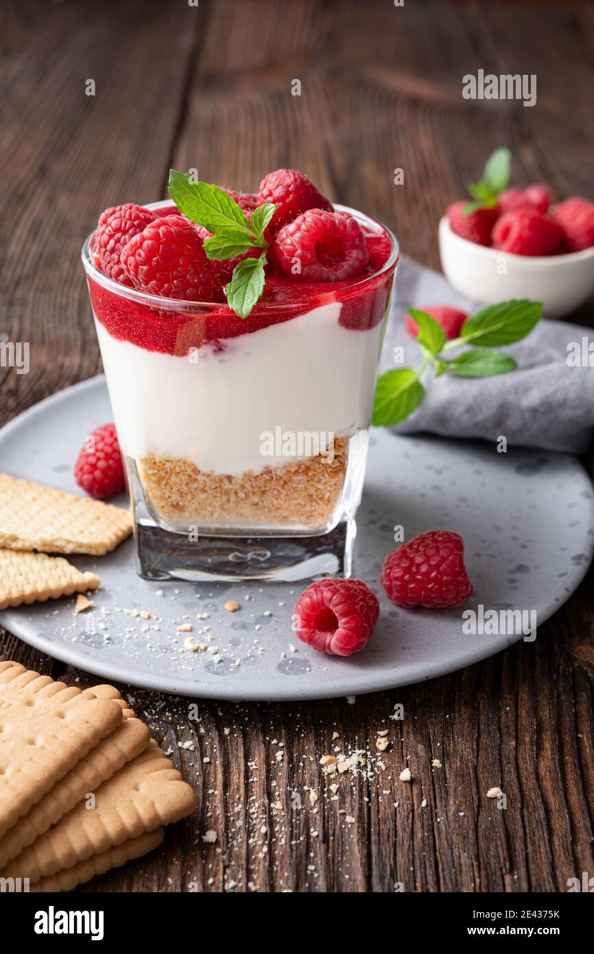 No bake cheesecake dessert in a glass jar topped with raspberry puree and fresh berries on rustic wooden background Stock Photo