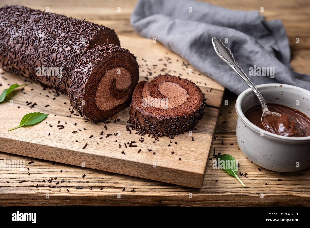 Chocolate cake roll with cocoa filling, topped with ganache glaze and sprinkles on wooden background Stock Photo