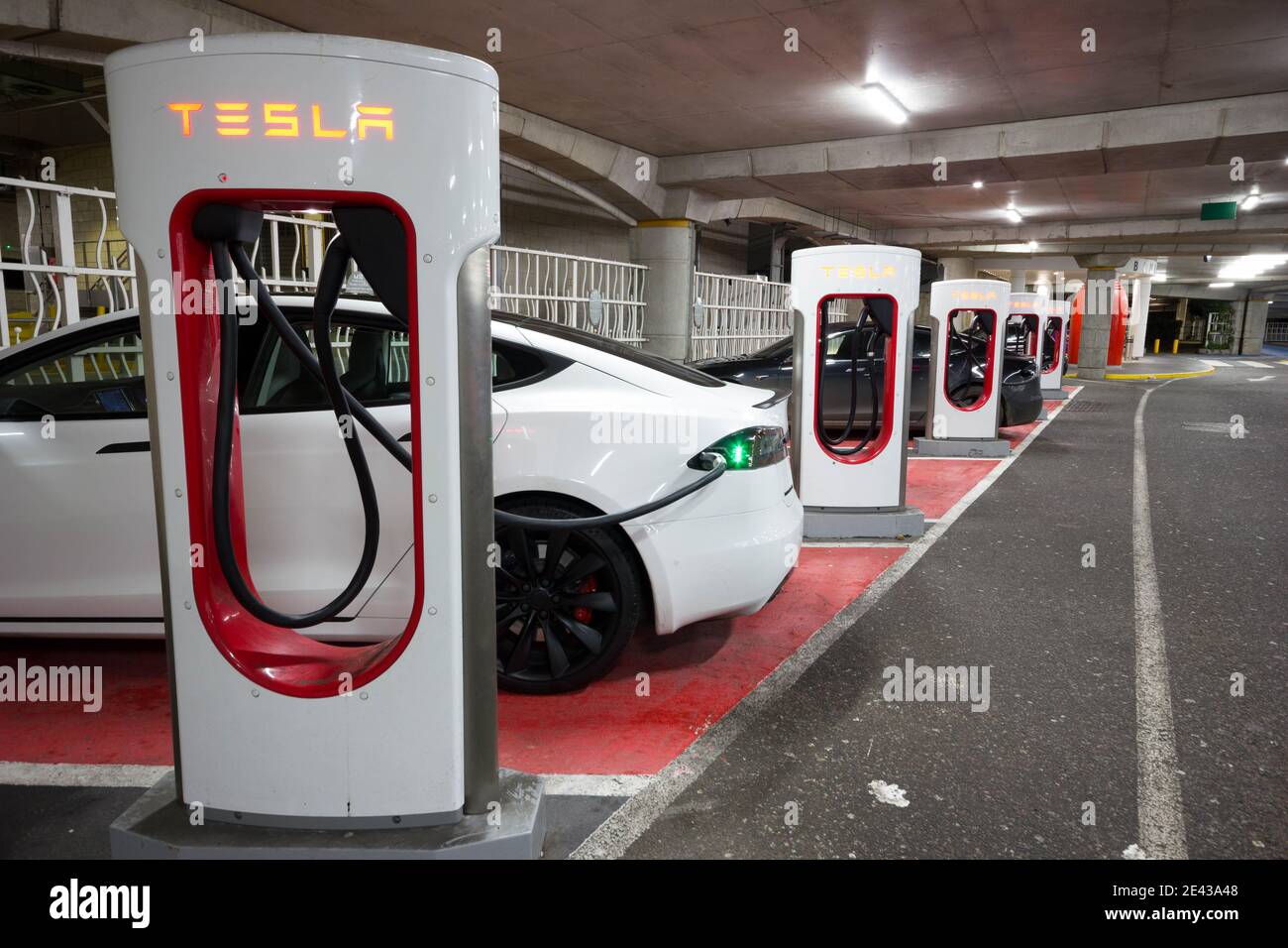 electrical car plugged into Tesla charging stations  in under cover car park, Kent, England Stock Photo