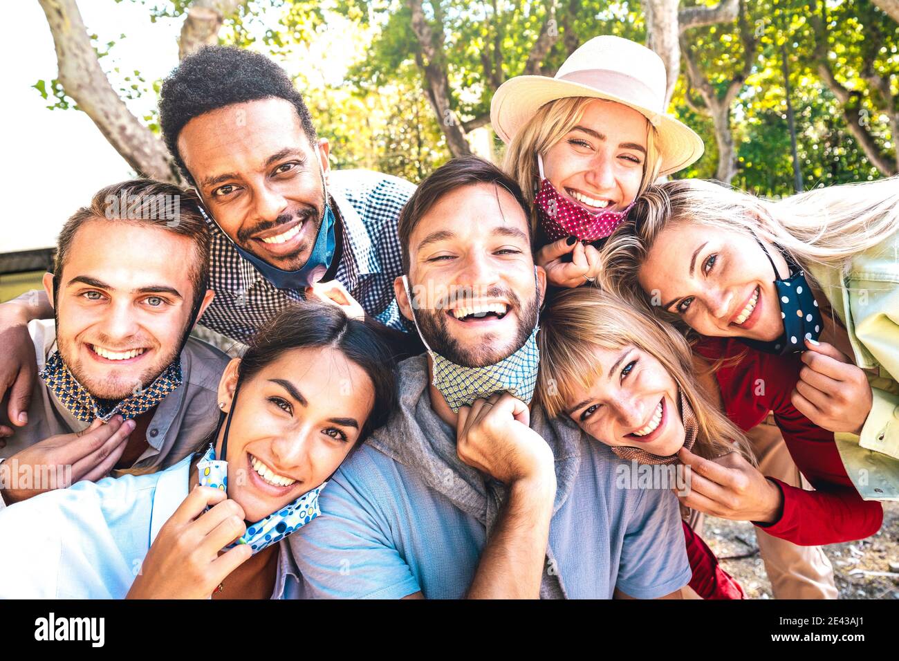 Multiracial friends taking happy selfie with open face masks after lockdown reopening - New normal friendship concept with young people having fun Stock Photo