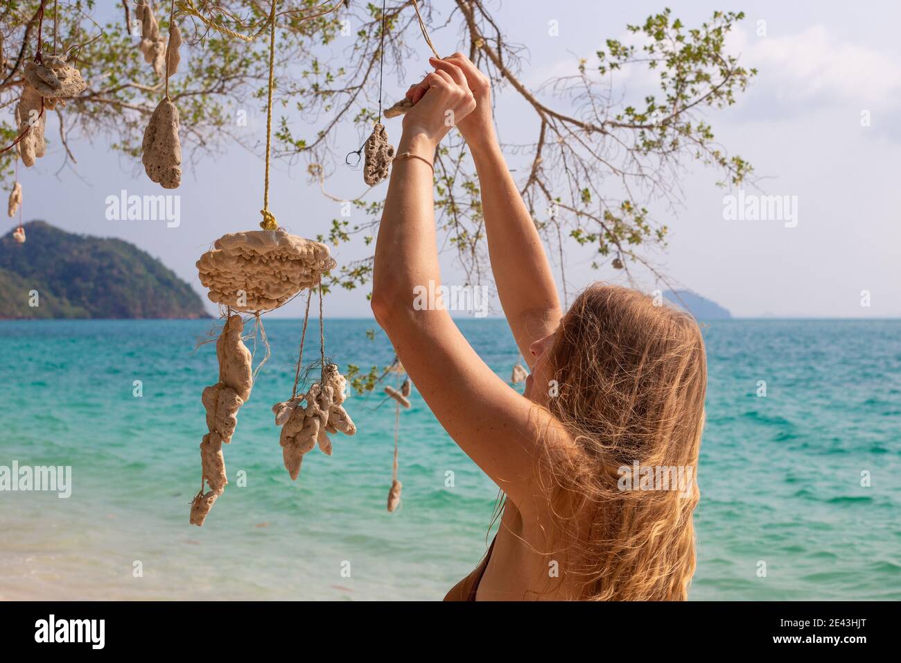 a woman with blond golden hair hangs corals on a wish tree, on the seashore, a dream come true Stock Photo