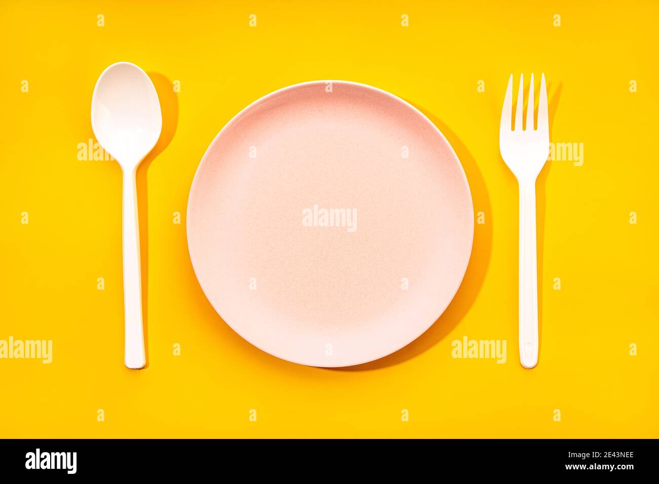 Top view composition with white plastic spoon and fork arranged near empty plate on yellow background Stock Photo