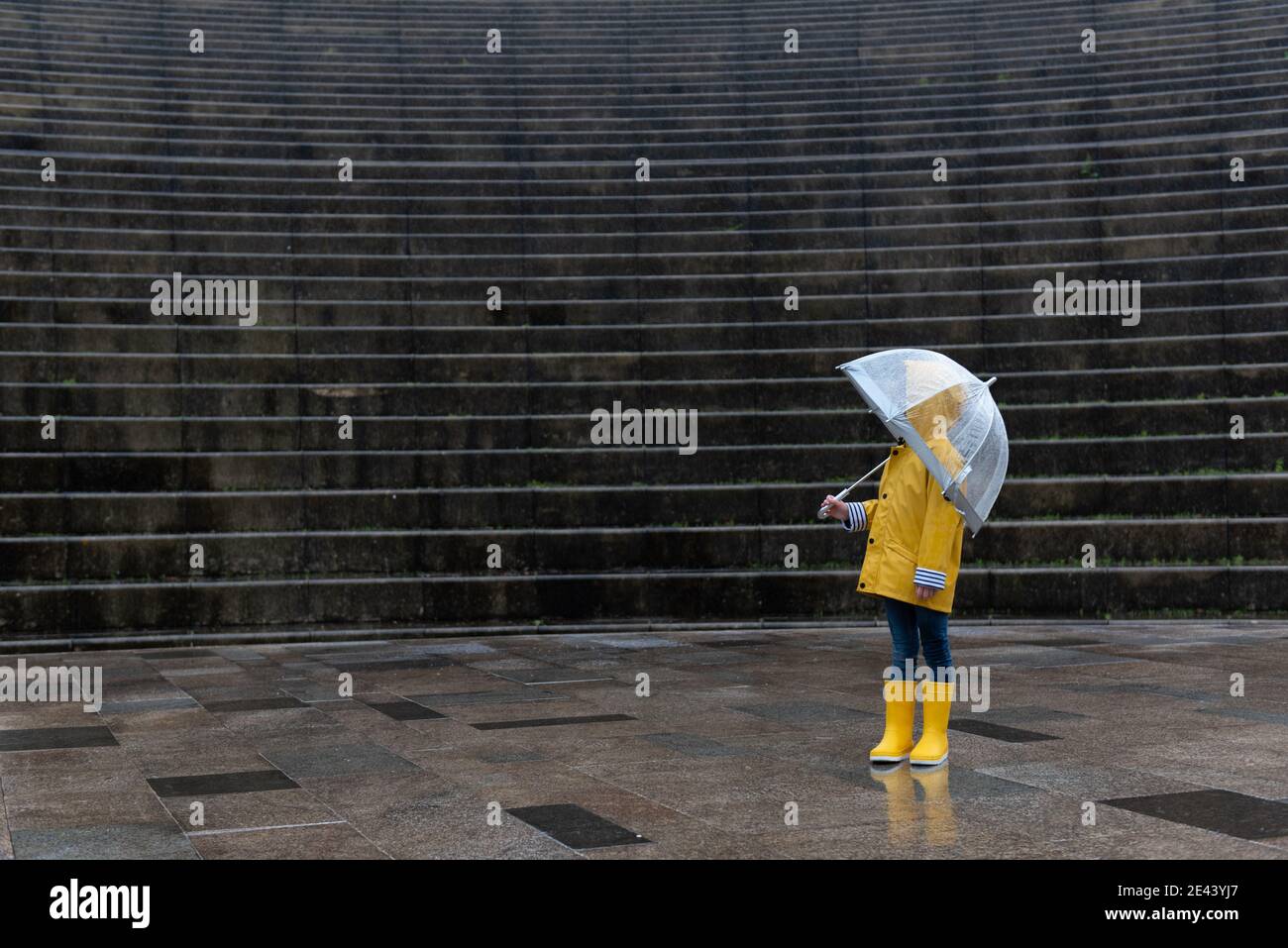 Side view of kid in yellow raincoat and with wet umbrella standing on