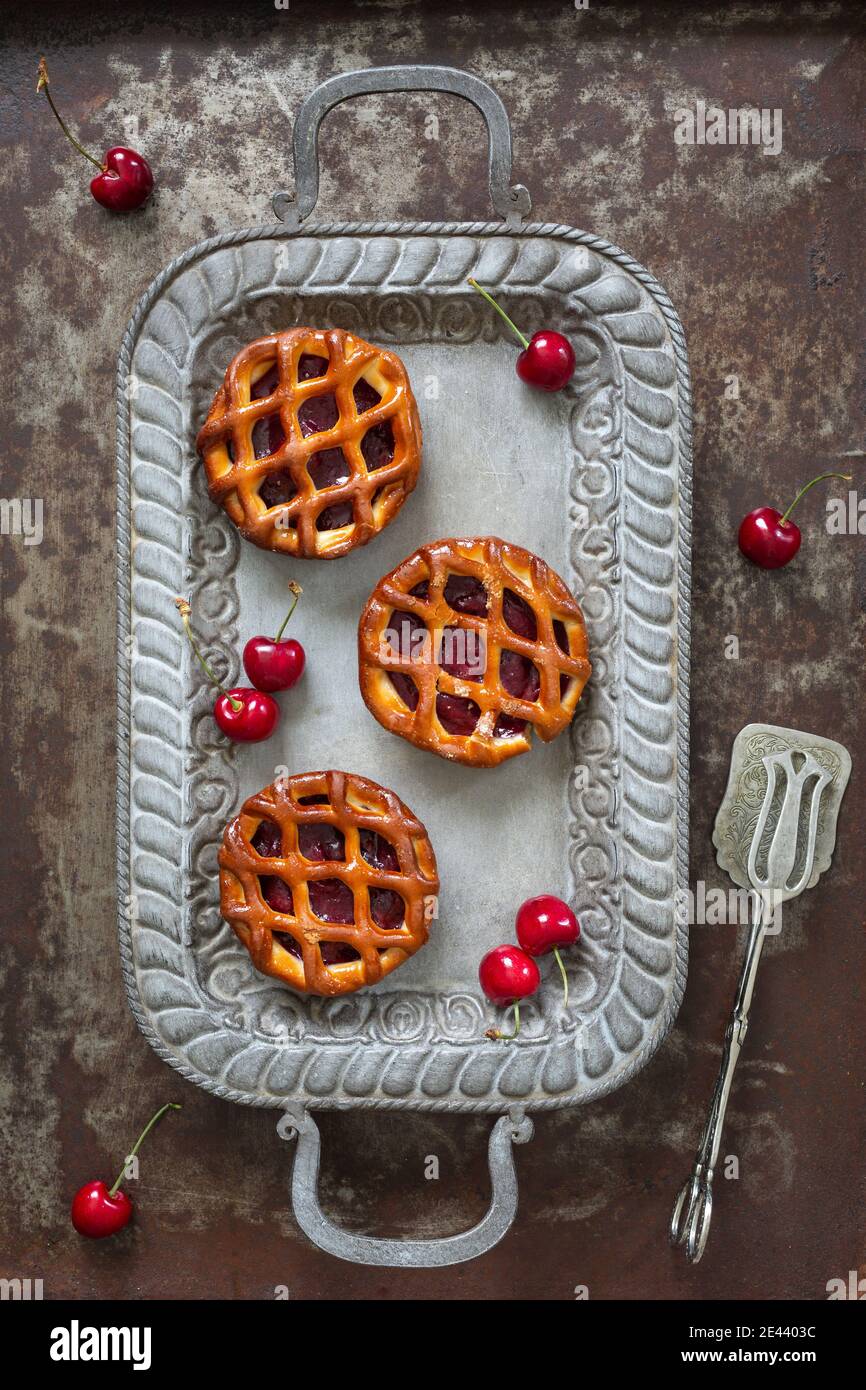 High angle view of three cherry pies and fresh cherries on a serving tray on rustic background Stock Photo