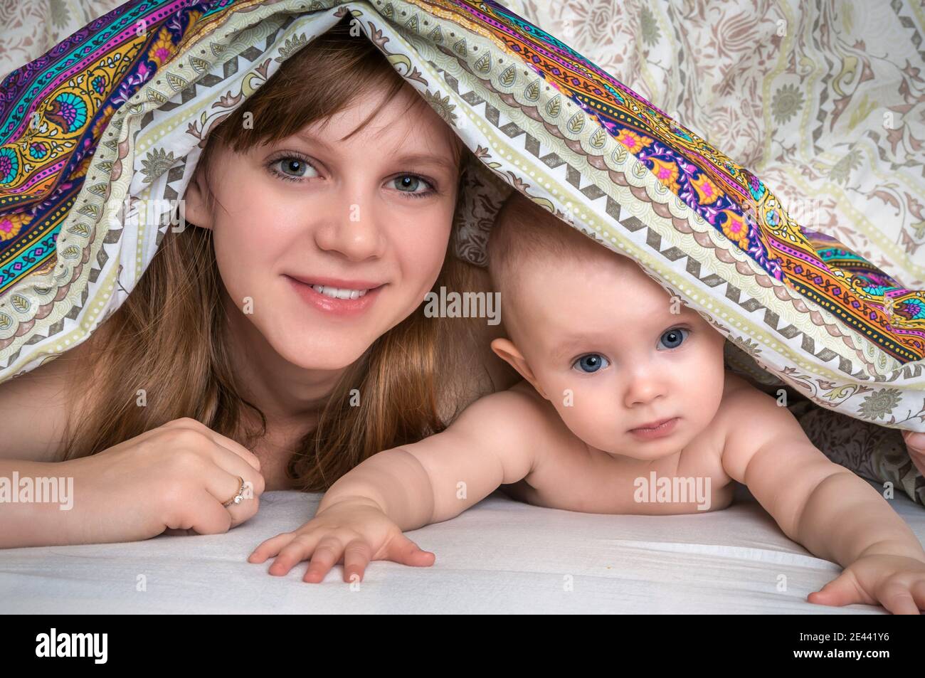Mother and her baby playing and smiling under a blanket in bed happy