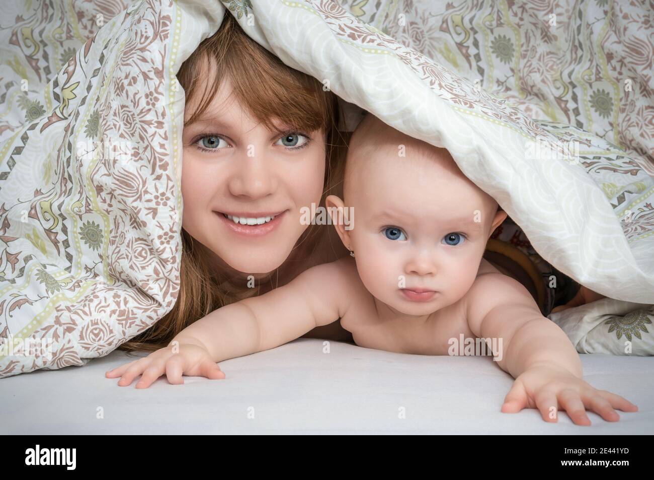 Mother and her baby playing and smiling under a blanket in bed happy