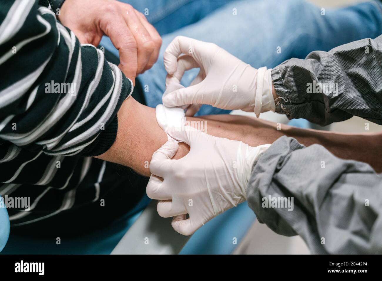 High angle side view of crop anonymous nurse in latex gloves applying patch on arm of patient after performing blood test in clinic Stock Photo