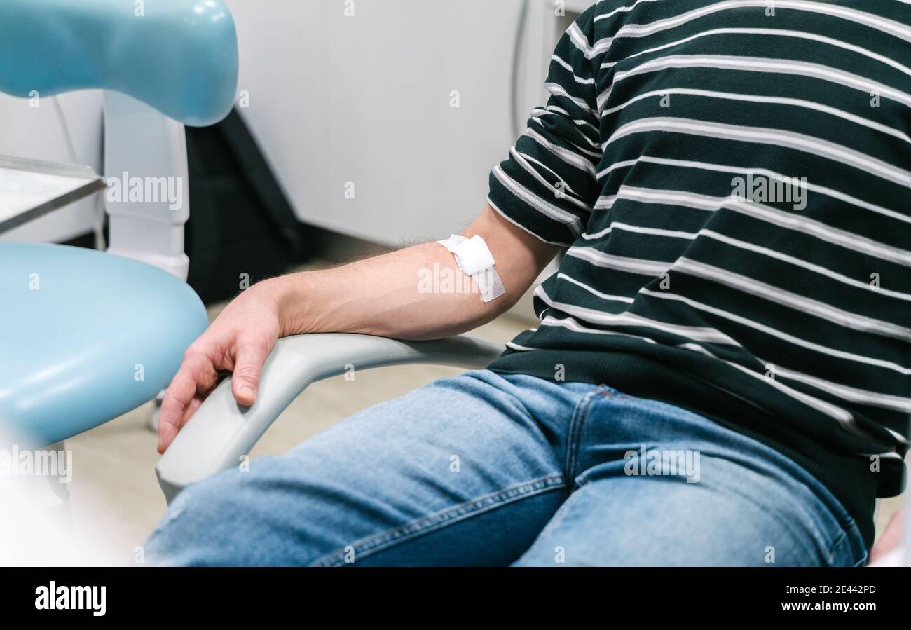 Crop anonymous patient with patch on arm sitting in chair after procedure of blood collection in modern lab Stock Photo
