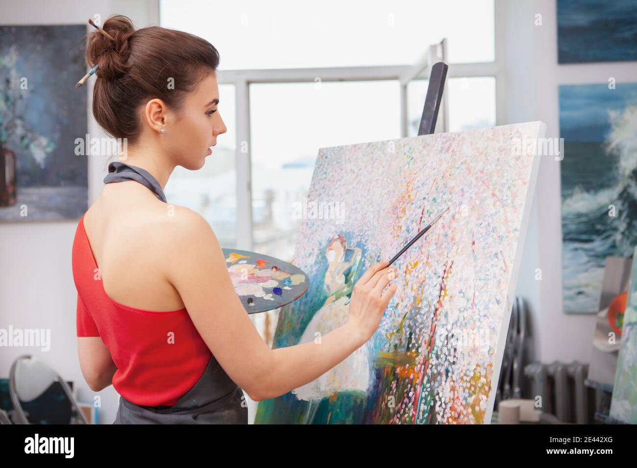 Artist Rearh Rear view shot of a young female artist working on a painting at her ...