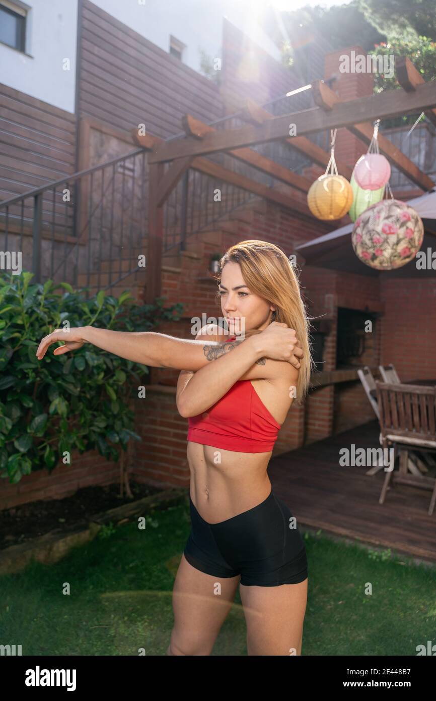 Focused female athlete doing stretching body while warming up before workout in backyard Stock Photo