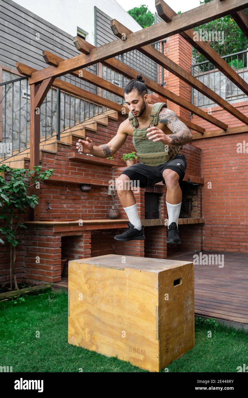 Fit male athlete with weight vest jumping on wooden box during active workout in backyard Stock Photo Alamy