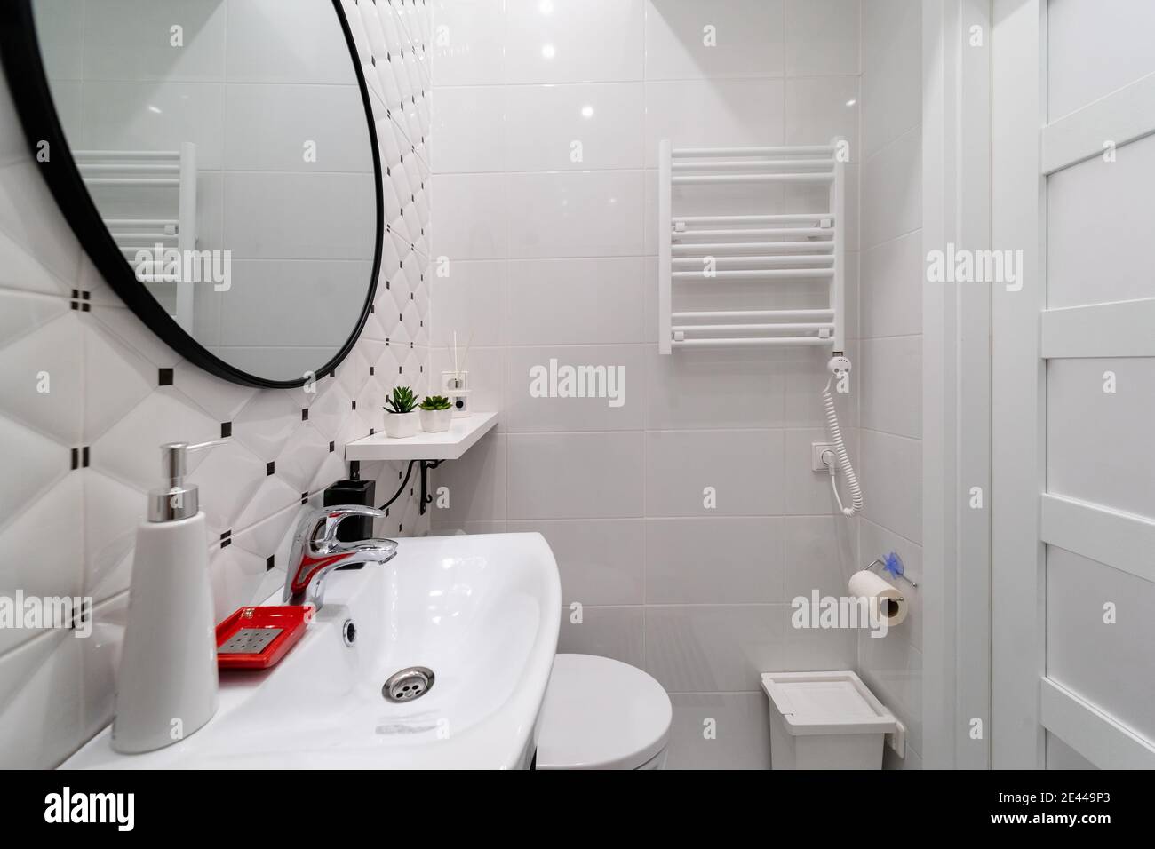 A part of a modern small bathroom in a newly furnished studio apartment in an old house. Ceramic tiled walls, towel radiator on white wall, sink, mirr Stock Photo