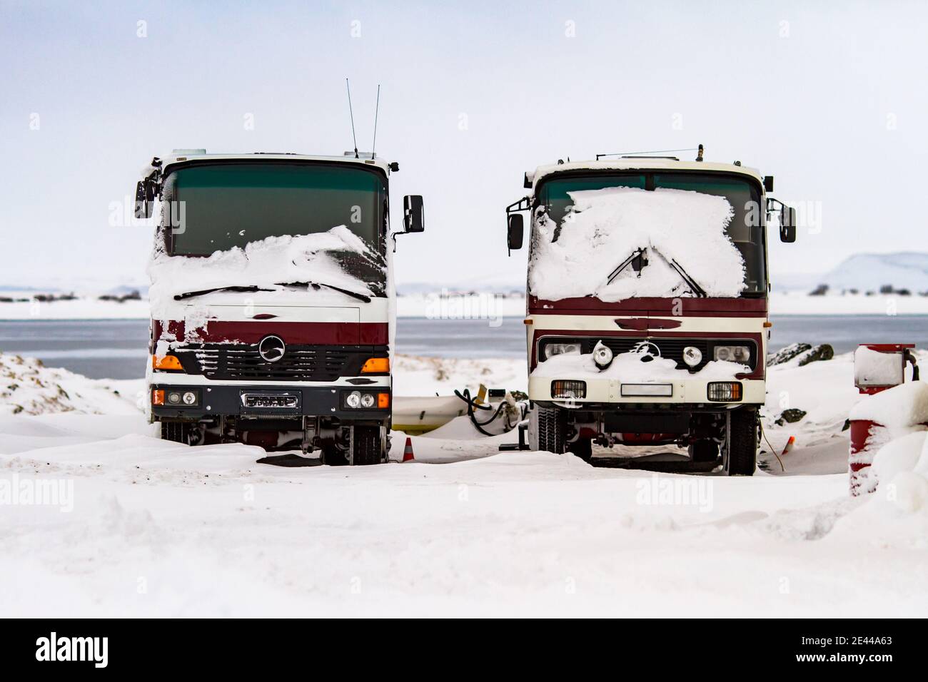 Red trucks covered with snow parked on background of sea in winter in Iceland Stock Photo