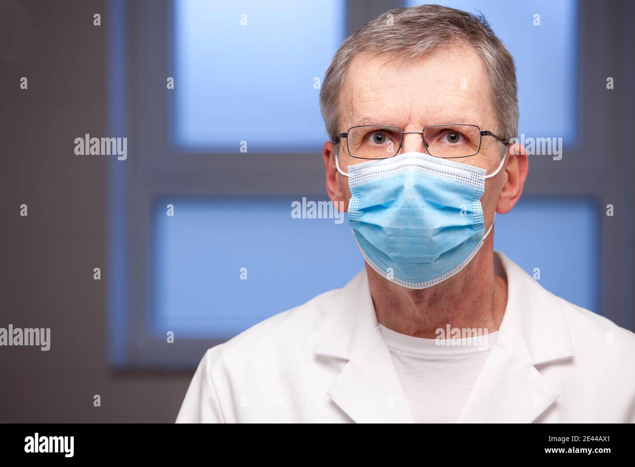 Portrait of mature doctor with surgical mask and white clothing looking at the camera - focus on the eyes Stock Photo
