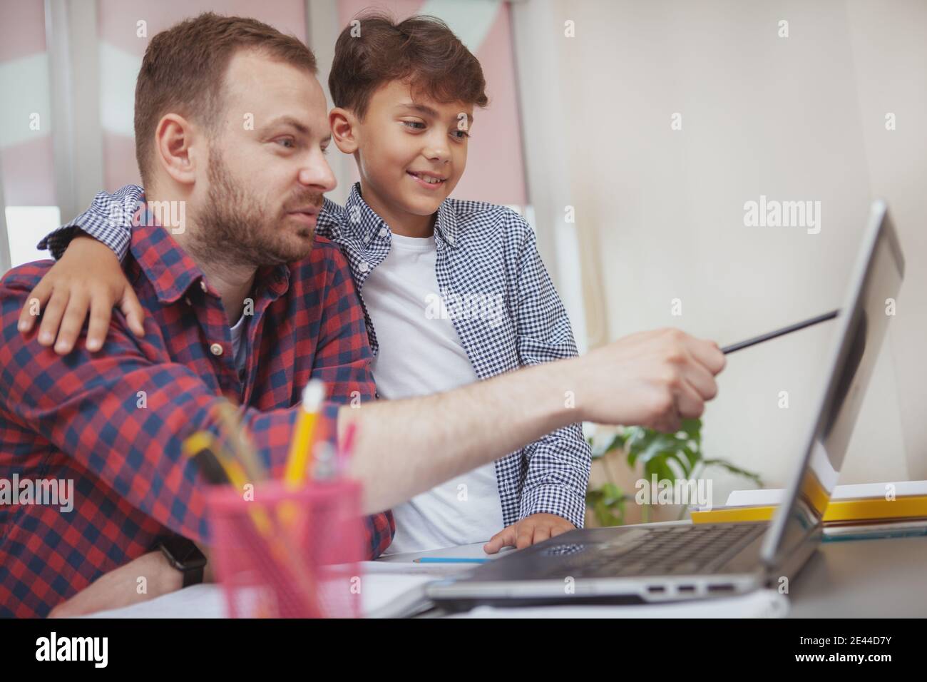 Young boy embracing his teacher while working on laptop together at ...
