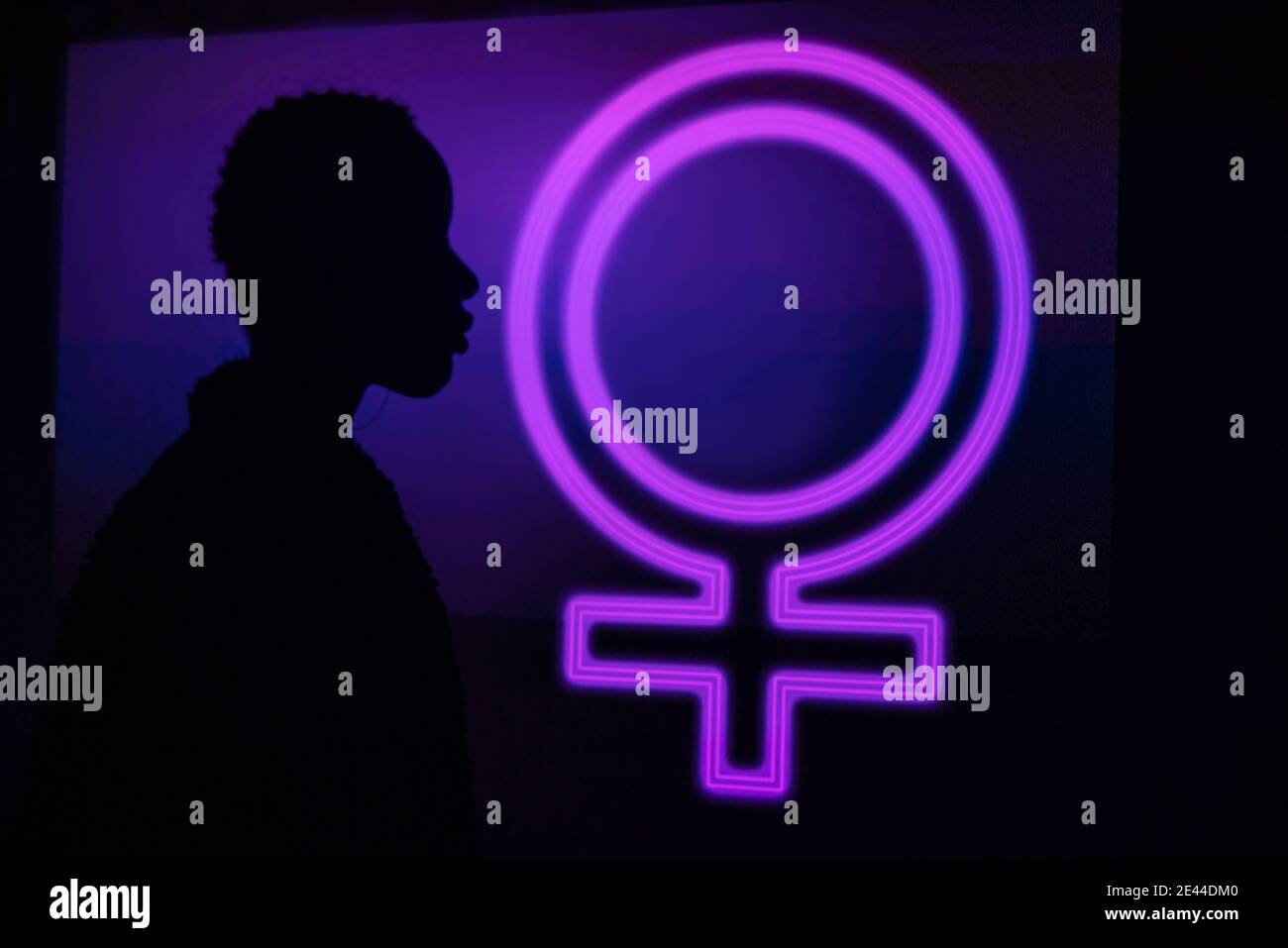 Side view of unrecognizable trendy black model silhouette standing near neon female symbol glowing with purple light Stock Photo