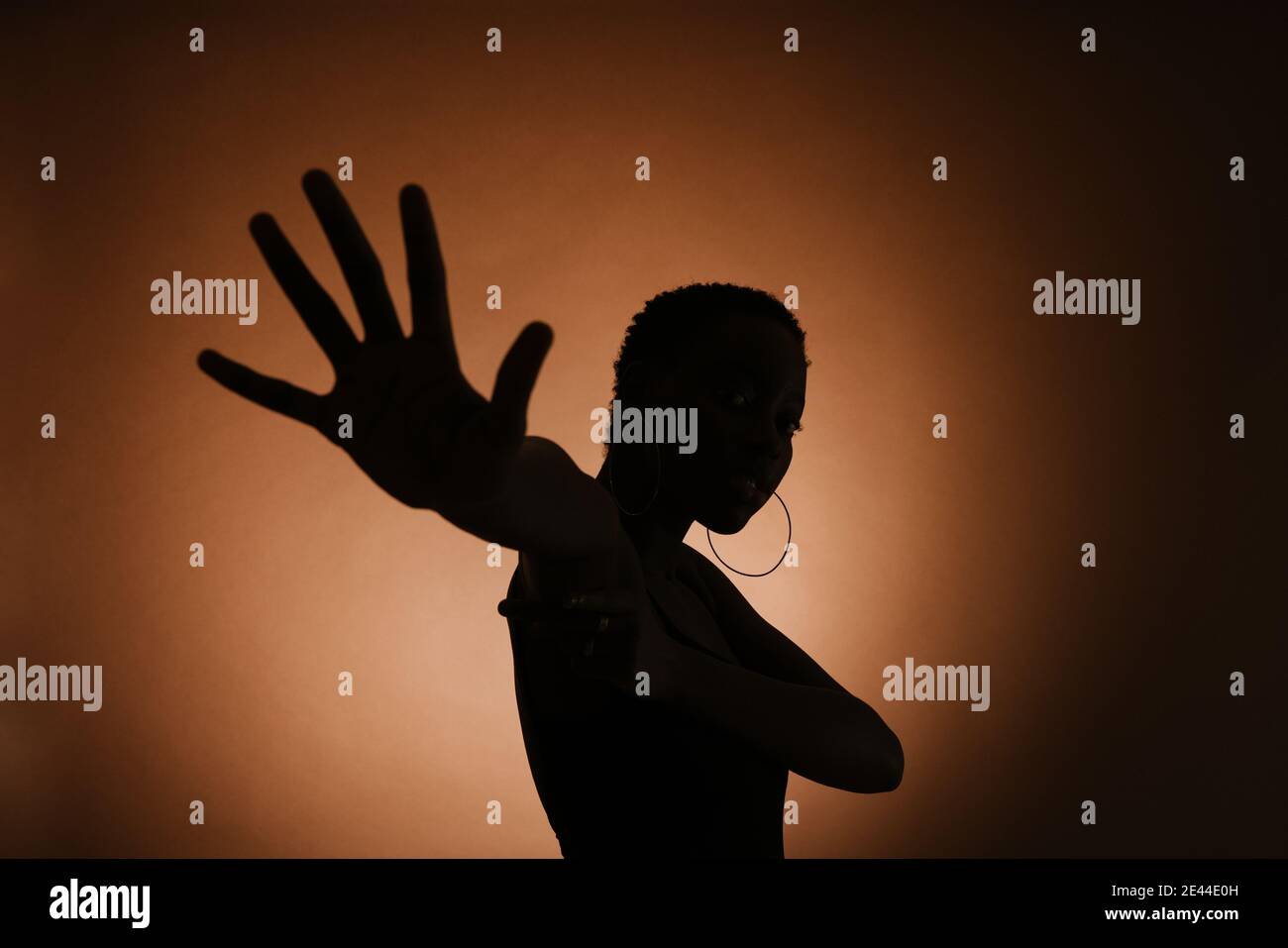 Silhouette of unrecognizable slender female making protective gesture against brown background Stock Photo