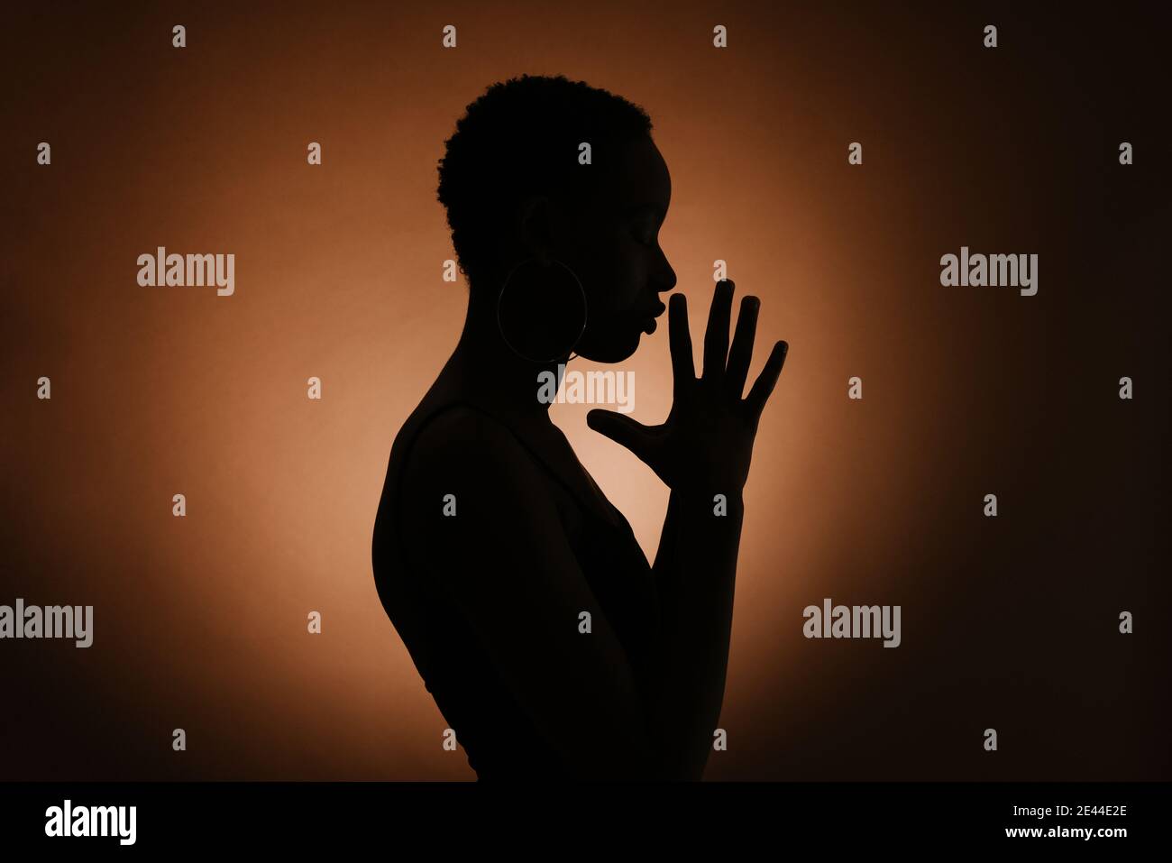Silhouette of anonymous ethnic female clasping hands and praying against brown background Stock Photo