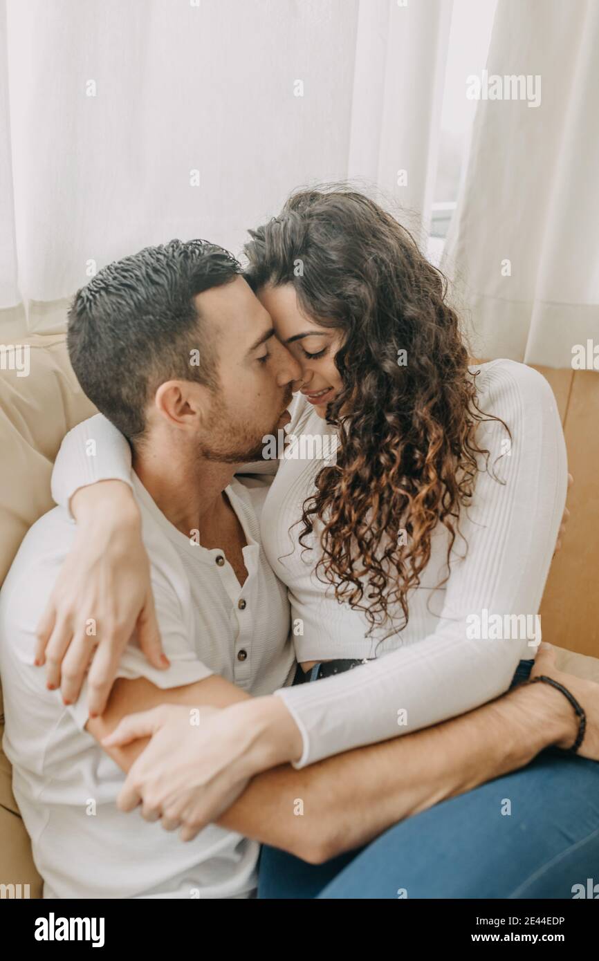 Loving couple sitting on soft sofa and tenderly hugging while ...