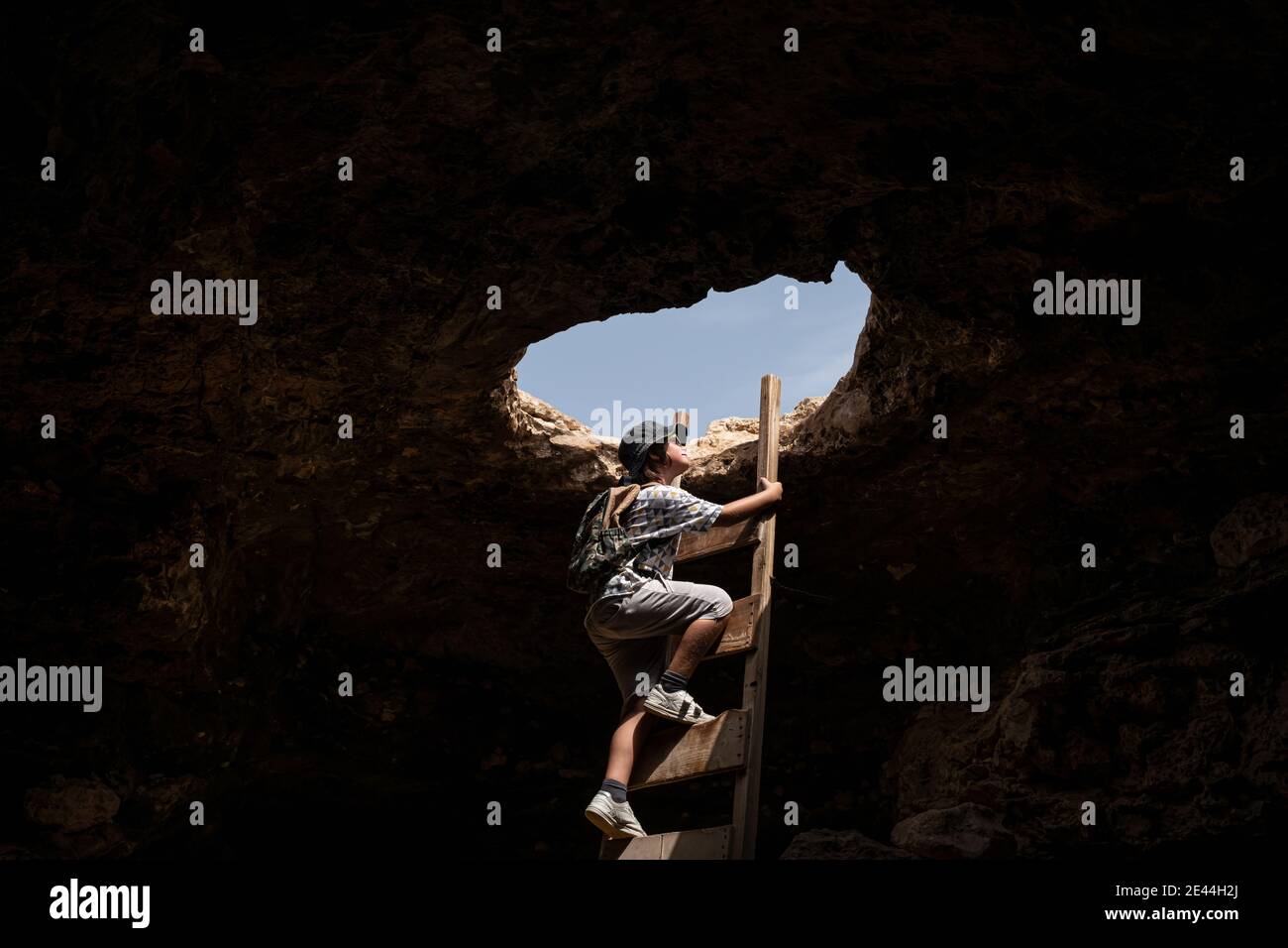 boy exploring a cave while climbing stairs through a hole Stock Photo
