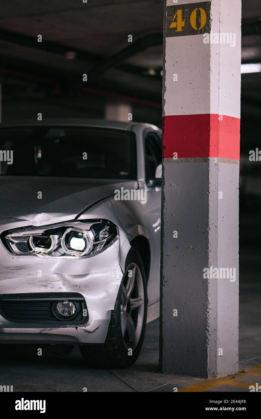 Modern silver car with damaged bumper parked near concrete column after  accident in garage Stock Photo