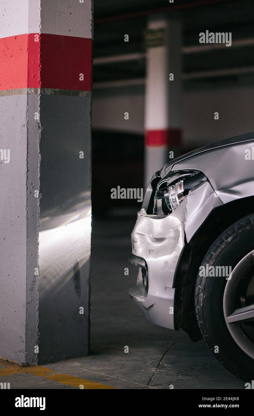 Modern car with broken headlight and damaged bumper parked near concrete column after accident in garage Stock Photo