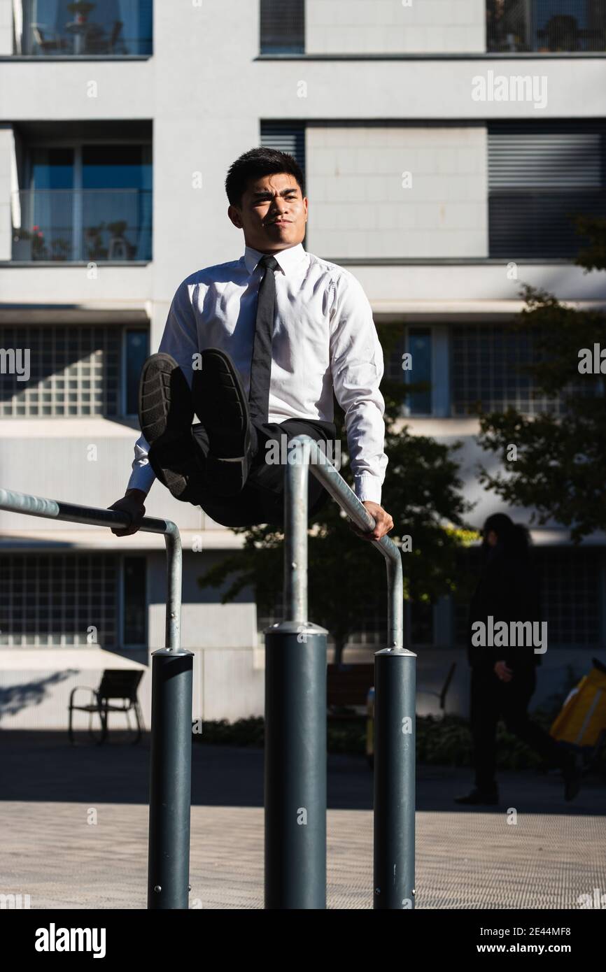 Asian male entrepreneur in formal outfit balancing on parallel bars while  doing abs exercises and grimacing Stock Photo - Alamy