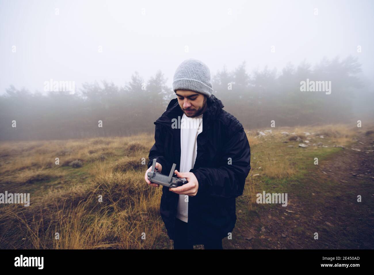 Male operating drone with remote controller while standing on path in foggy field in autumn Stock Photo