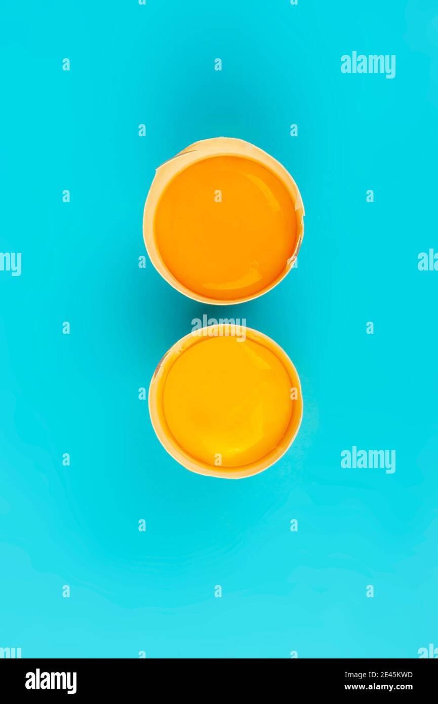 Two raw chicken egg yolks in broken shells vertical on blue background Stock Photo
