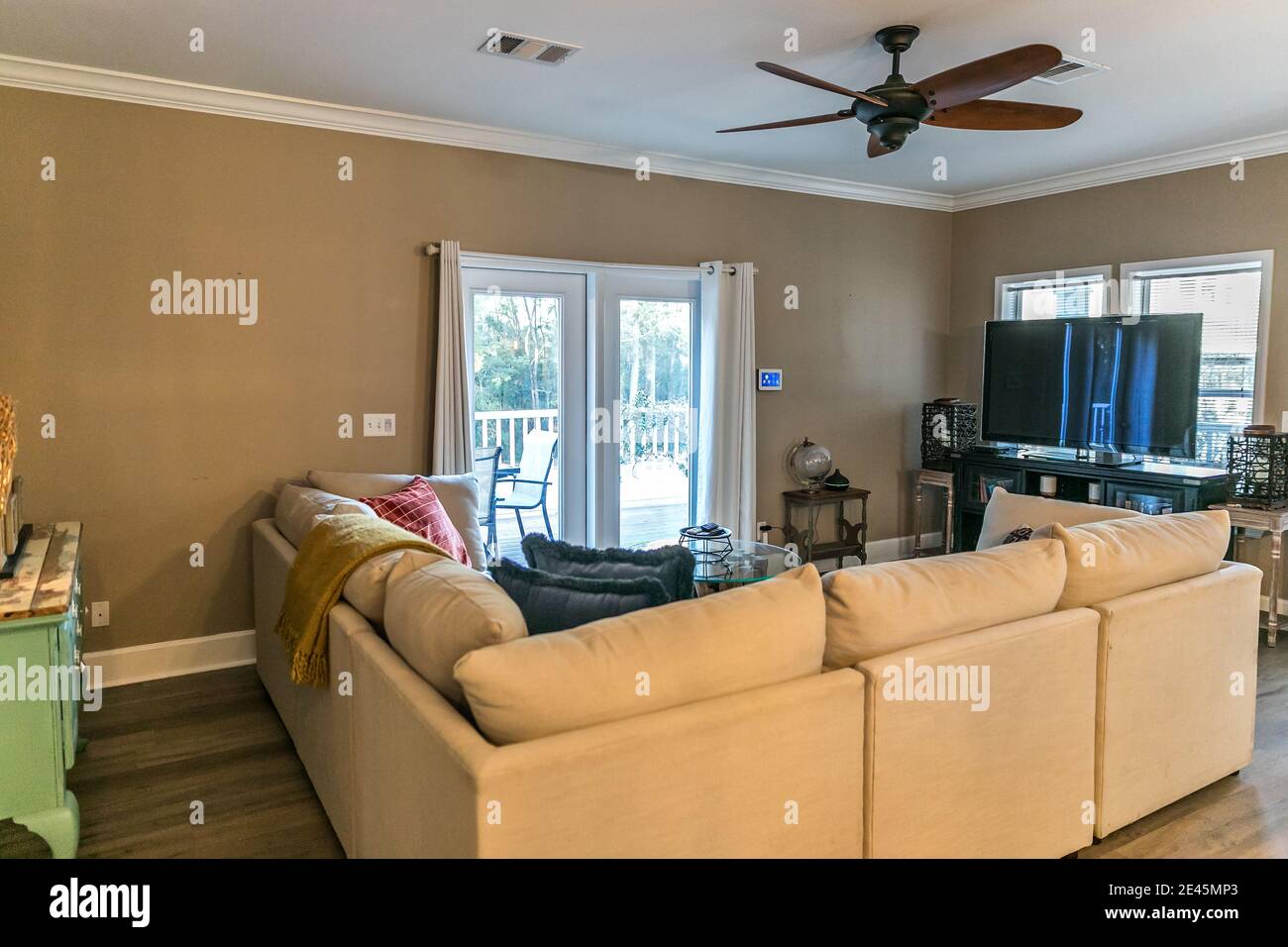 Small living room with a cream colored couch and a television and a fan